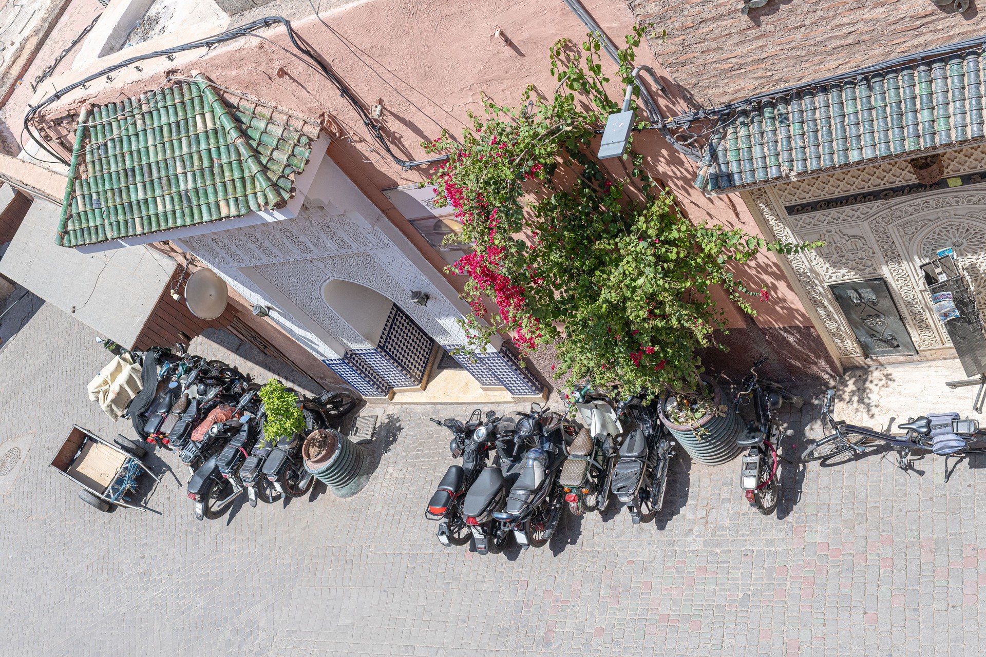 Des motos et des vélos garés bordent une ruelle étroite de Marrakech, au Maroc, mettant en valeur l’architecture marocaine traditionnelle et les bougainvilliers animés